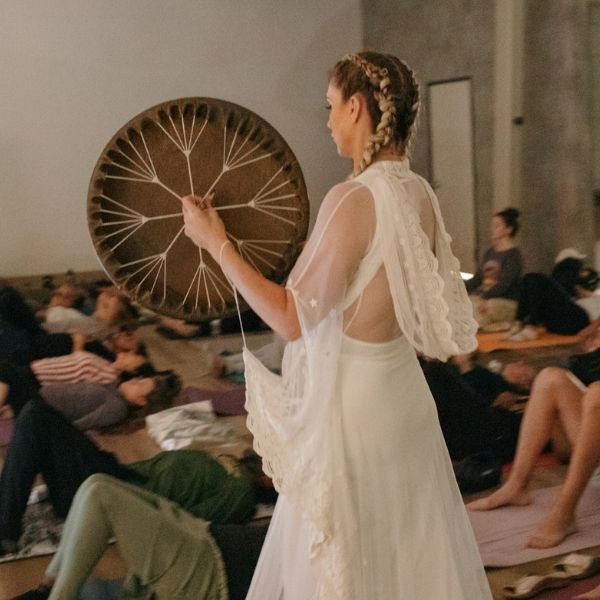 A facilitator plays a drum during a Live Community REset Experience, using rhythmic vibrations to guide participants through a transformative sound healing session.