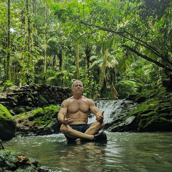 Damon Damato meditating in a tranquil jungle stream, surrounded by lush greenery during The Healing Sanctuary’s Tropical Retreat in Costa Rica.