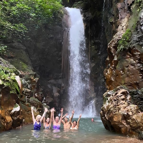 Guests swimming in a crystal-clear waterfall pool, surrounded by the lush Costa Rican jungle during The Healing Sanctuary’s Tropical Retreat.