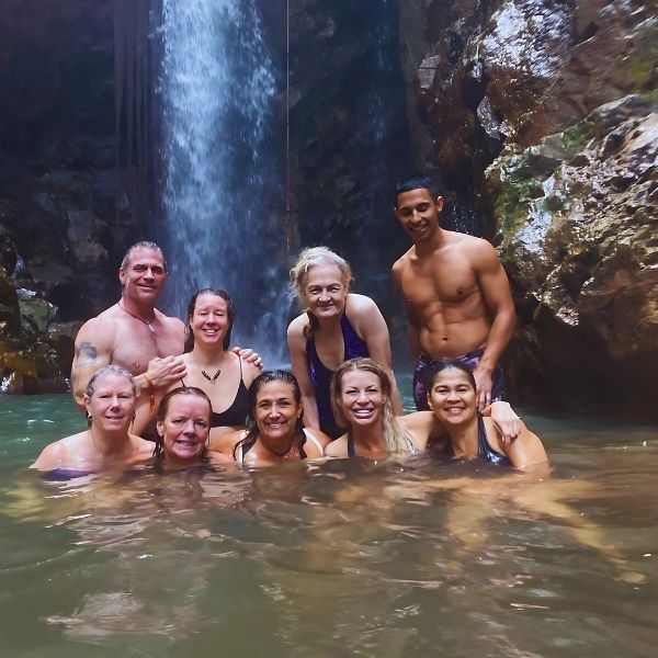 Guests swimming beneath a breathtaking waterfall in the lush Costa Rican jungle during The Healing Sanctuary’s Tropical Retreat, embracing nature and rejuvenation.